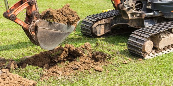 Gravemaskin som graver på gressplen